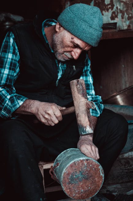 Elderly artisan meticulously hammering a metal object indoors, showcasing craftsmanship.